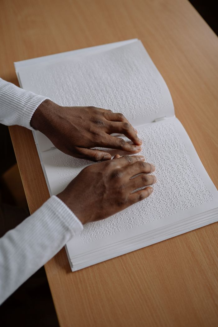 About A pair of hands reading a Braille book on a wooden table, highlighting accessibility.
